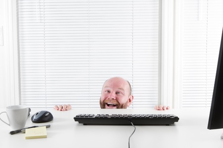 Strange and happy Office worker looking up from under his desk  Hiding behind his desk の写真素材