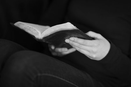 A black and white close-up of a christian woman folding hands and praying on the bible 