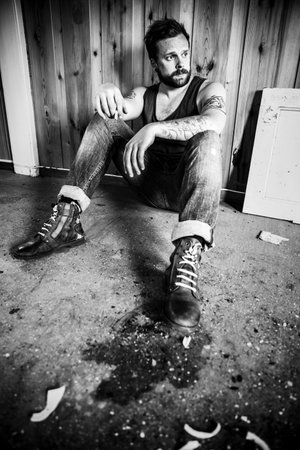 Punk rocker or redneck sits on the floor and smoke in a messy house 