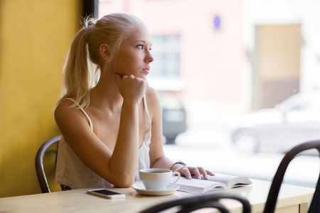 Pensive young woman at cafe looks out the windowの写真素材