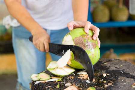 Asian woman chops fresh coconut with a big knife at a market in Penang, Malaysia.の写真素材