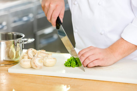 Close-up of a professional chef chopping parley and muschroom in the large kitchen.の写真素材