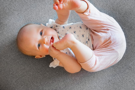 Cute baby girl with blue eyes laying on the sofa holding her foot.