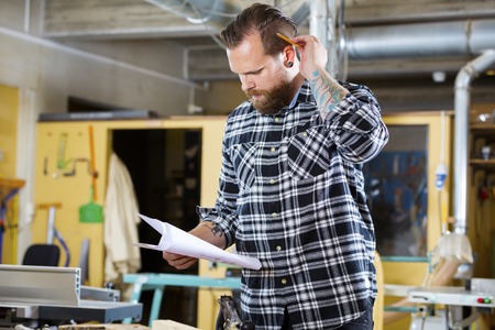 Adult craftsman looks at drawing in a work shop for wood work and construction. Carpenter designs and prepares new work.の写真素材