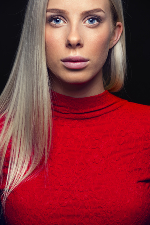 Fashion photo of a beautiful young woman with blonde hair in a red dress on black background. Natural retouched studio portrait.の写真素材