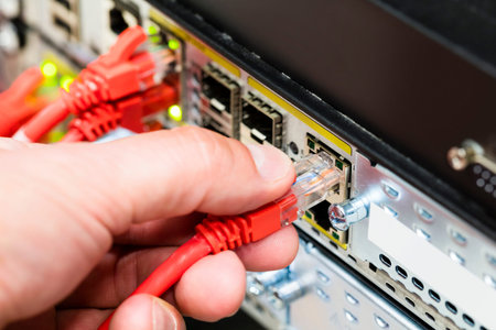 Closeup of male technician's hand plugging fiber cable into switch or router in datacenter