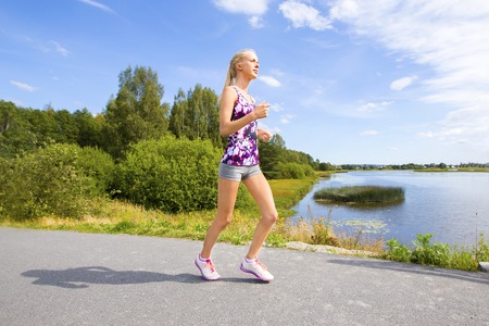 Beautiful young slim blonde woman running or jogging on a bridge along the water. Workout a summer evening.の写真素材