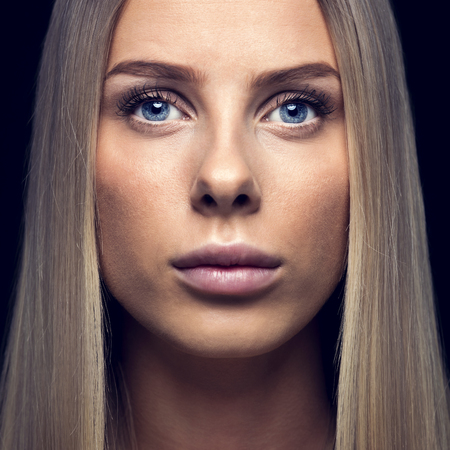 Closeup portrait of beautiful young woman with blond hair over black backgroundの写真素材