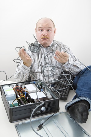Portrait of confused businessman holding tangled cables of computer at desk in officeの写真素材