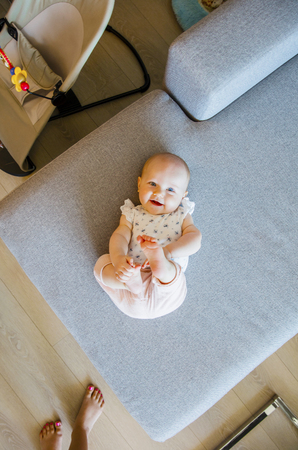 Cute baby girl with blue eyes laying on the sofa holding her foot.の写真素材