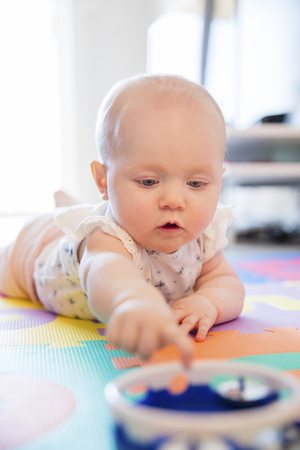 Baby girl with blue eyes playing on the floor with toys on a playmat. A cute young child plays.の写真素材