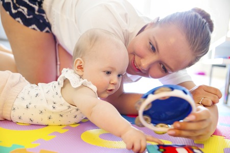 Happy and caring mother laughing together with her child. Smiling and cute young baby girl playing on mat.の写真素材