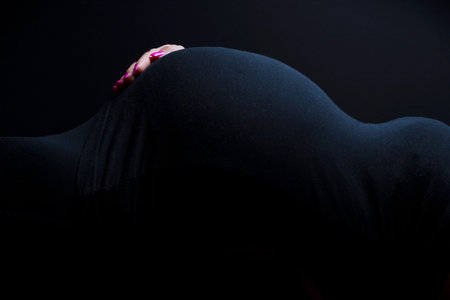 Side view of a beautiful young pregnant woman body shape with a hand on the tummy on black...
