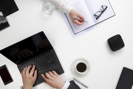 Businessman Using Laptop While Female Colleague Writing In Diaryの写真素材