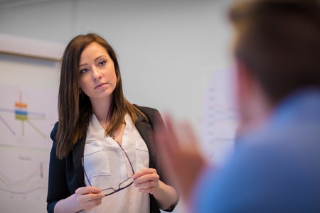 Businesswoman Holding Eyeglasses While Looking At Colleagueの写真素材