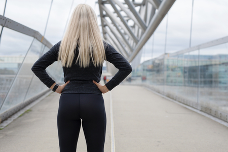 Fit blonde woman runner standing on bridge in modern looking cityの写真素材