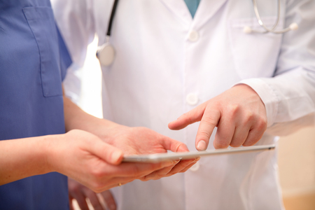 Doctor and nurse discussing patients tests at tablet computer in hospitalの写真素材