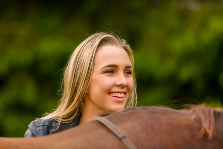 Close-up of smiling woman patting her arabian horse with grass in the fieldの写真素材