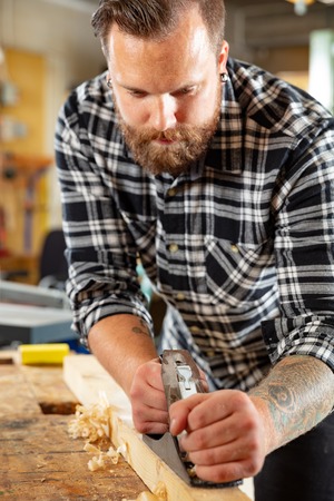 Carpenter work with planer on wood plank in workshopの写真素材