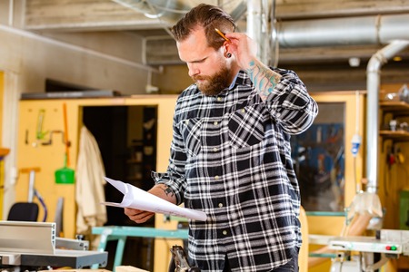 Carpenter planning work and looking at drawings in the workshopの写真素材
