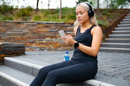 Beautiful sports woman sitting at stairs listen to music from smartphoneの写真素材
