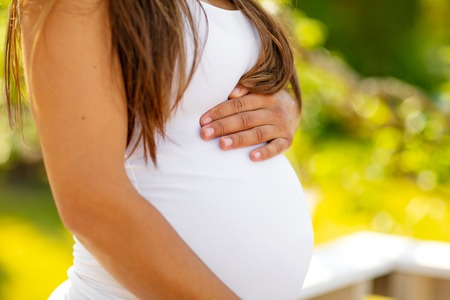 Mid-section of pregnant woman standing outdoor holding hands on bellyの写真素材