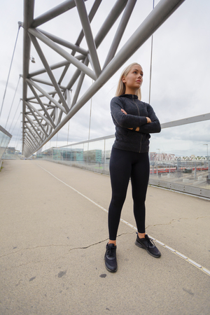 Confident Woman in Black Workout Wear Standing At Modern Bridge In Cityの写真素材