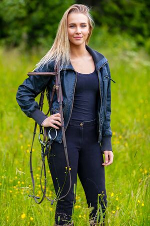 Beautilful young female horse rider standing in a green meadowの写真素材