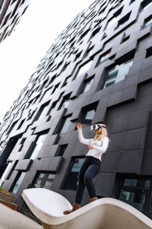 Woman Wearing Virtual Reality Glasses Standing Between Futuristic City Buildingsの写真素材