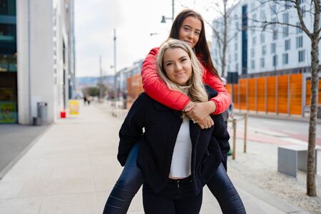 Smiling Female Friends Having Fun and Piggybacking In City Environmentの写真素材