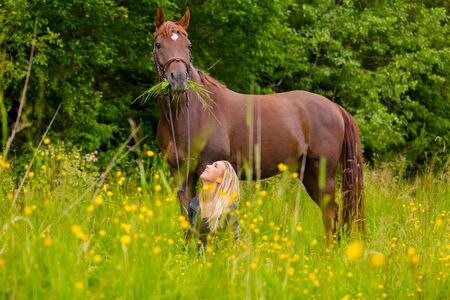 Smiling woman sitting in the meadow and communicate with her arabian horseの写真素材