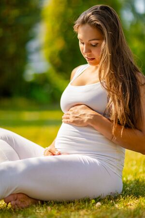 Happy pregnant woman sitting on the grass in a beautiful gardenの写真素材