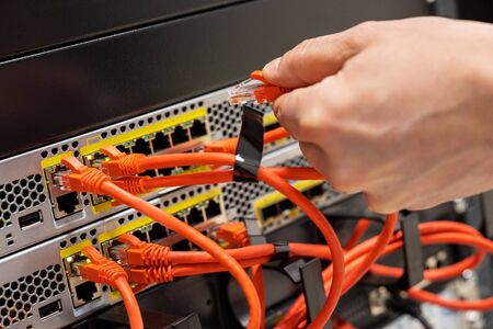 Male IT Engineer Plugging Network Cable In Router in Datacenterの写真素材