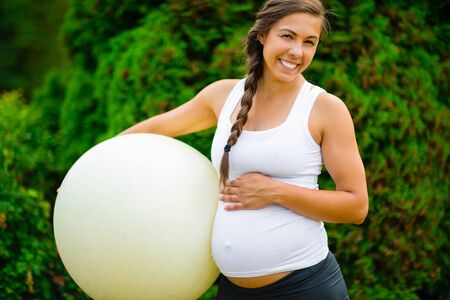 Portrait Of Pregnant Woman Touching Abdomen While Holding Fitness Ballの写真素材