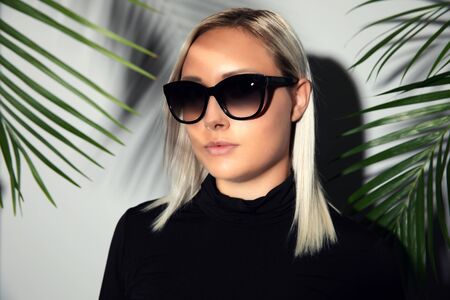Beautiful woman with sunglasses hiding behind tropical palm leavesの写真素材