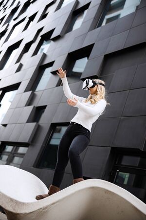 Young Woman Wearing Virtual Reality Glasses In Front Of Futuristic Buildingの写真素材