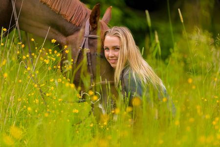 Smiling blonde woman sitting in the meadow with her arabian horseの写真素材