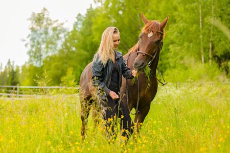 Smiling woman feeding her arabian horse with snacks in the fieldの写真素材