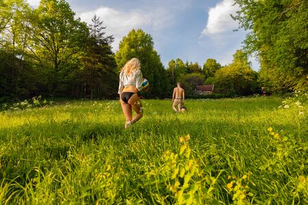 Rear view of young couple walking on grass in forest during summer vacation, Idyllic scenery with cabin in the background.の写真素材