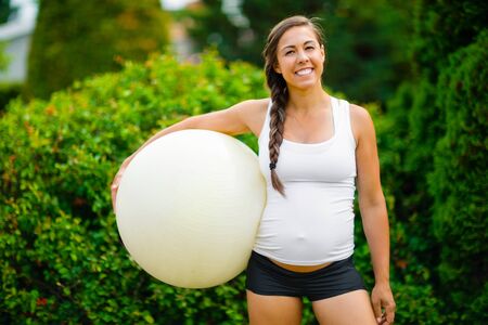 Smiling Young Expectant Mother Holding Exercise Ball In Parkの写真素材