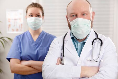 Portrait of confident doctor and nurse in surgical masks standing at clinic. Follow the instruction given for virus infection.の写真素材