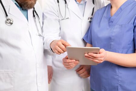 Doctor in medical team discussing patient report at tablet computer in hospitalの写真素材