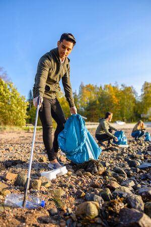 Man cleaning beach with volunteers on sunny dayの写真素材