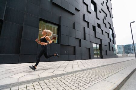 Fast running athletic woman wearing sports top in modern city environmentの写真素材