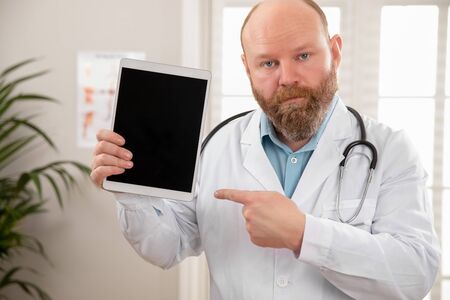 Serious adult male doctor showing a digital image or report on a tabletの写真素材