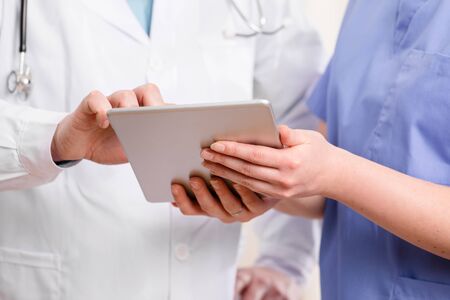 Doctor and nurse discussing tests or x-ray image about a patient at tablet computer in hospital. Technology in healthcare services.の写真素材