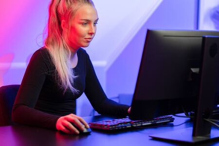 Focused Blonde Gamer Girl Playing Online Video Game on Her Personal Computer.の写真素材