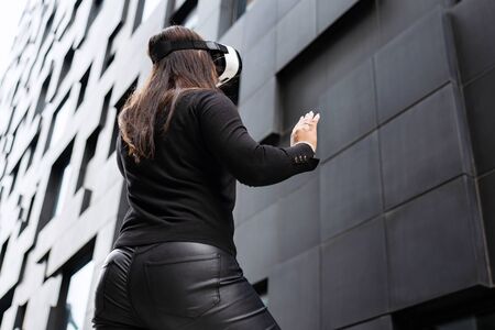 Back Of Woman Wearing Virtual Reality Technology Glasses Against Modern Buildingの写真素材