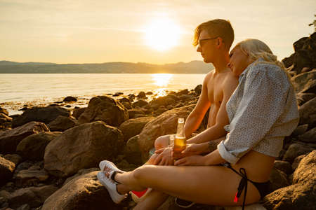 Couple relaxing and drinking beer at the beach at sunsetの写真素材