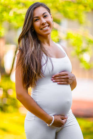 Smiling pregnant woman standing in garden holding on tummyの写真素材